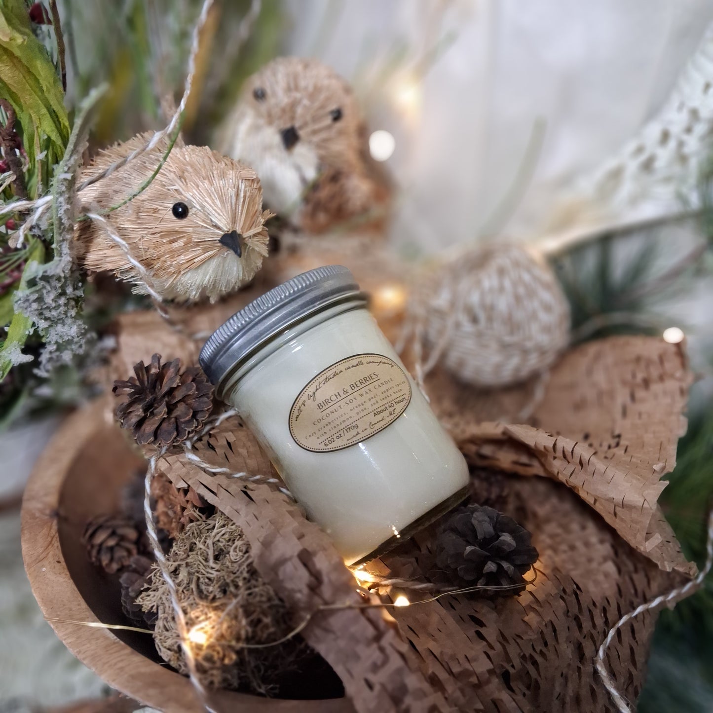 Birch & Berries Coconut Soy Candle in a decorative holder with birds, twine, and natural elements and string lights