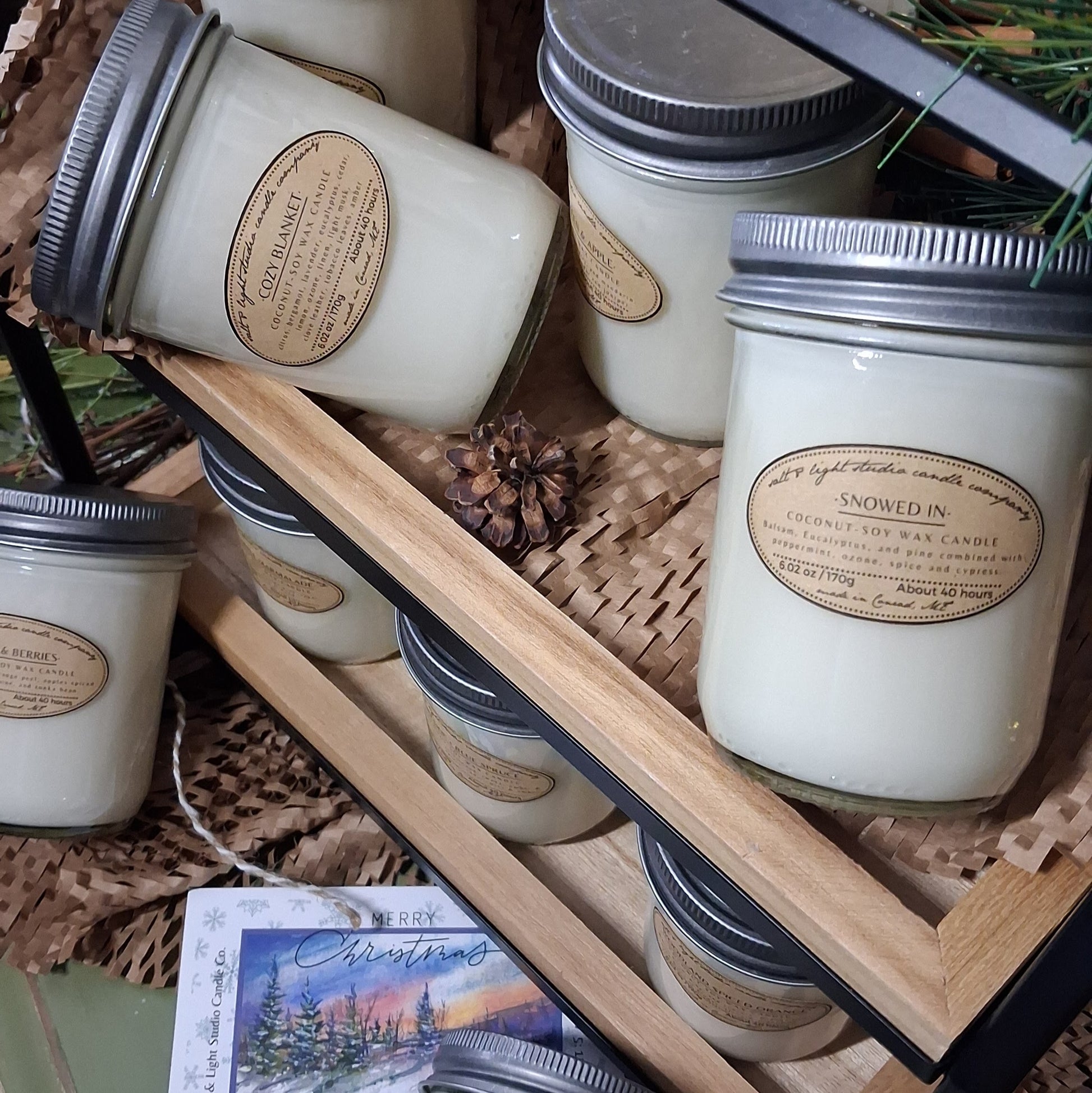 Jars of coconut soy candles in mason jars with labels on a farmhouse wooden tray with pinecones and greenery.