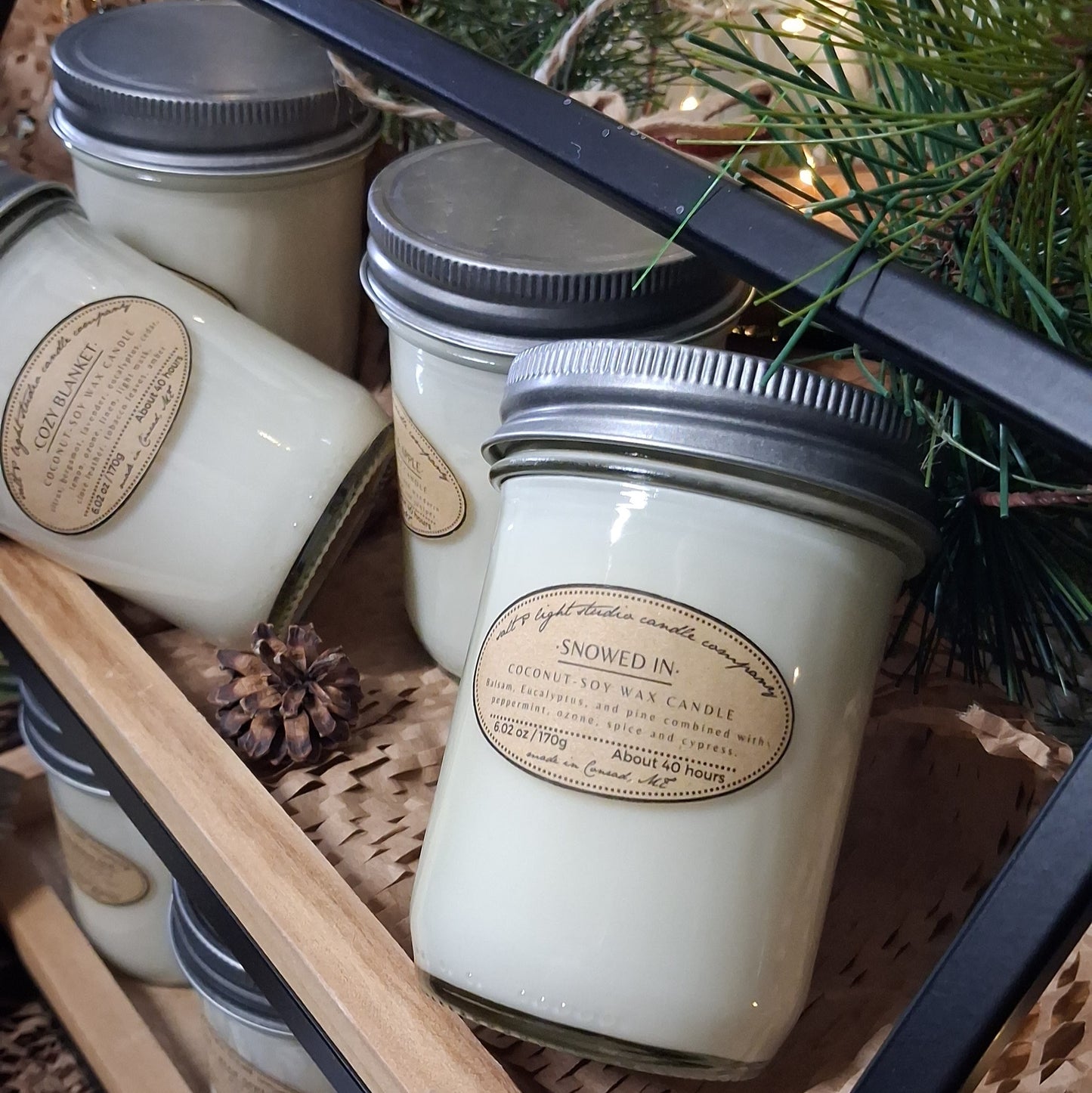 Mason jar artisan candles with seasonal scents on a wooden tray with pinecones and greenery
